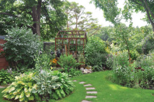 In the lush green beds of the backyard, the Victory Orangery greenhouse is barely visible.